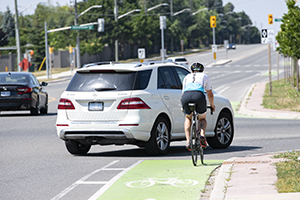 A cyclist rides in a green bike lane while a car turns in his path
