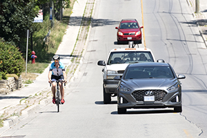 A cyclist rides near the curb while cars pass