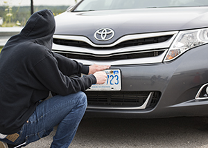 A person in a black hoodie holds a screwdriver near a licence plate