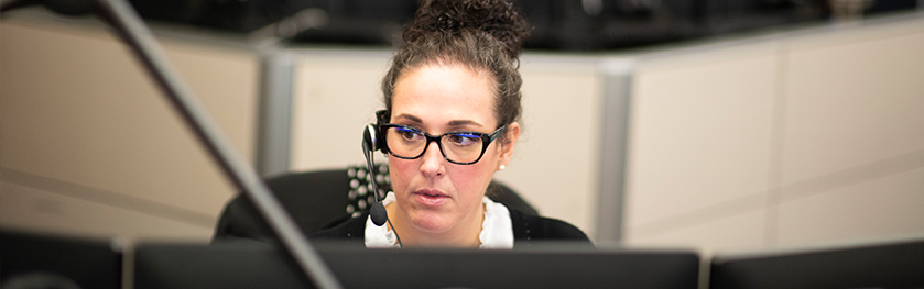 A woman wearing glasses and a headset looks at a monitor