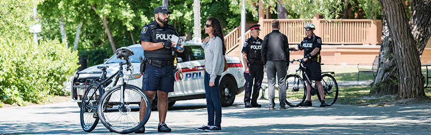 A group of people congregate in a park in front of police cruisers