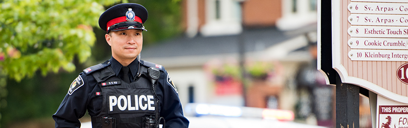 A man in a police uniform stands in front of a streetscape