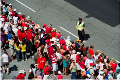 A male officer watches a crowd of people lined up on the side of a road