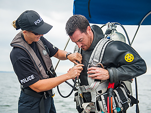 A woman helps a man adjust a black dive suit