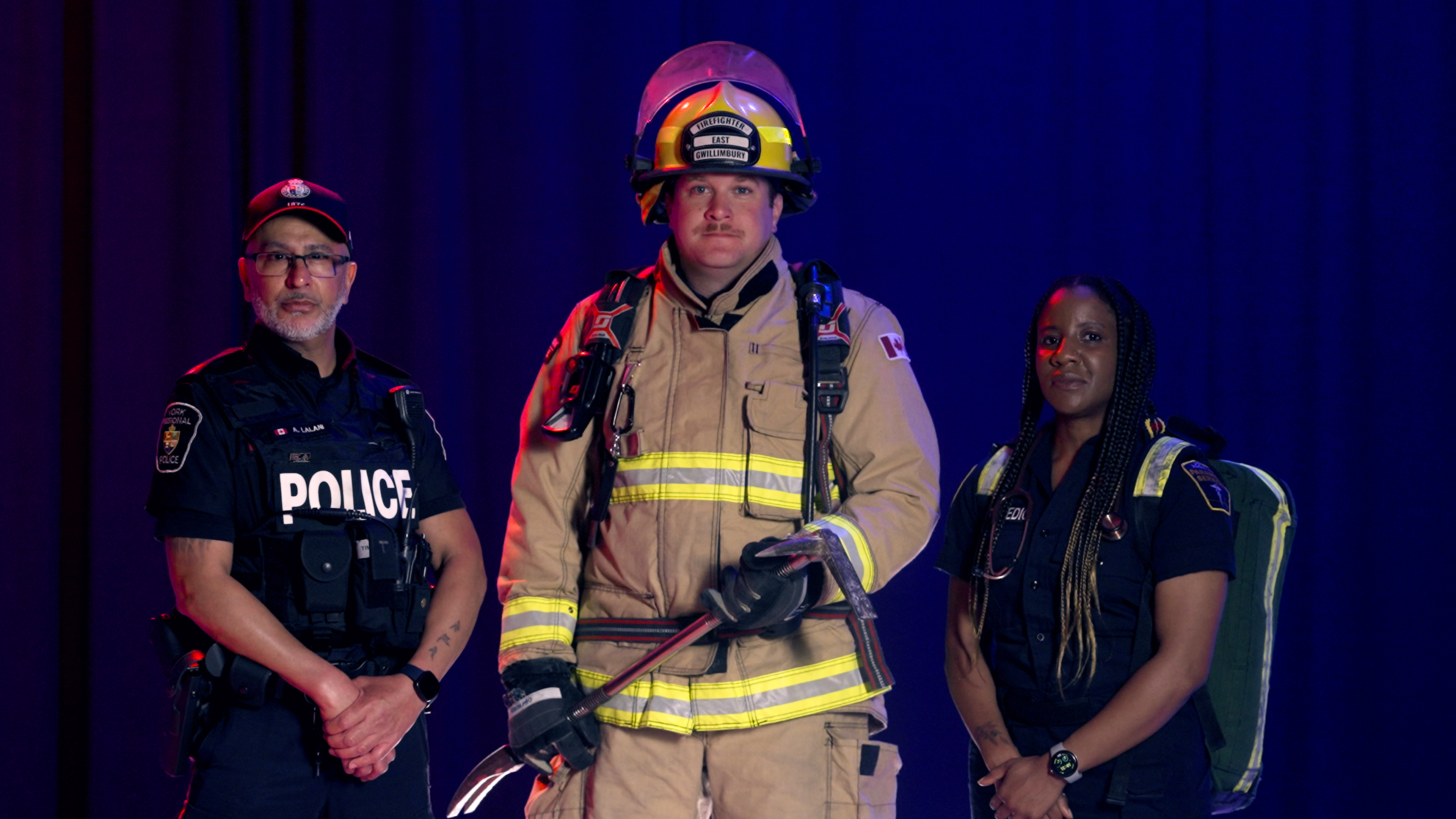 A male police officer, a male firefighter and a female paramedic pose against a blue backdrop