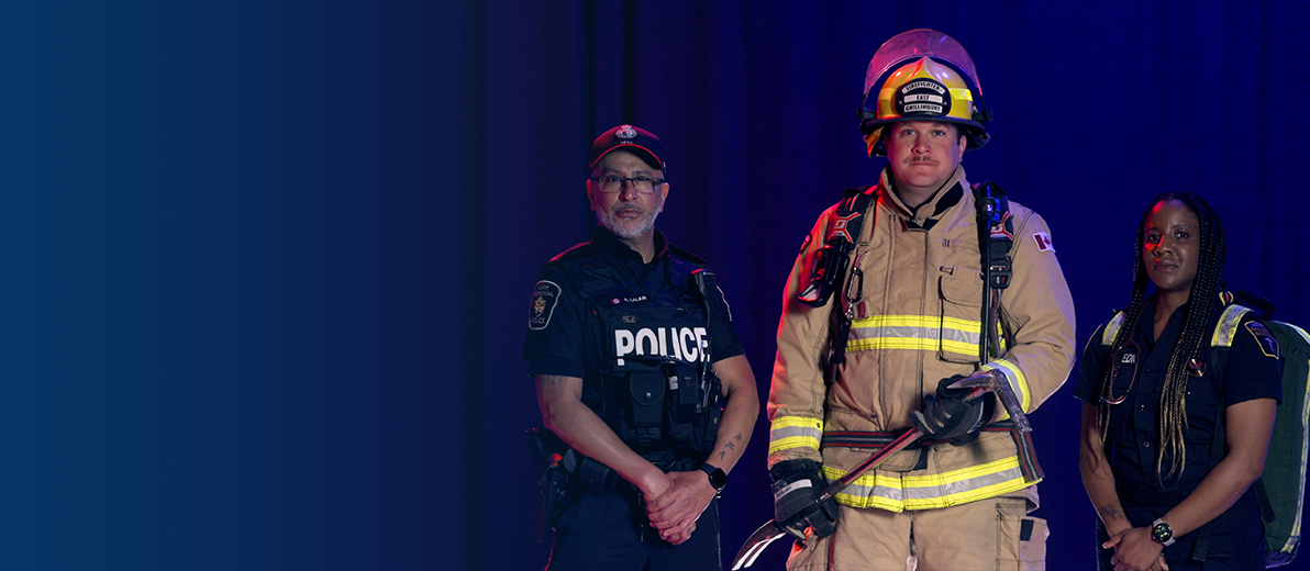 A male police officer, male firefighter and female paramedic pose, looking at camera