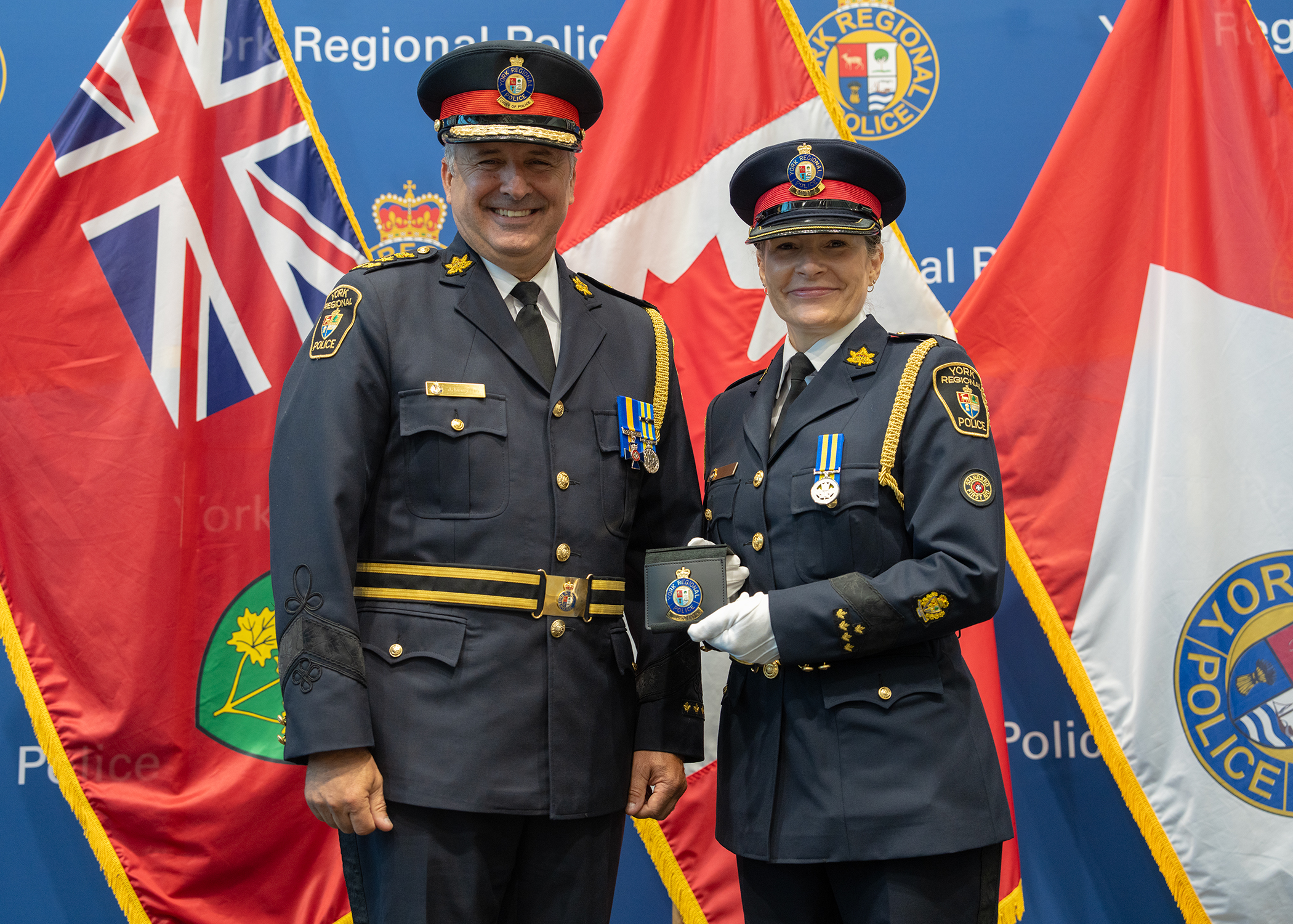 A male officer and a female officer stand in front of a flag pole smiling