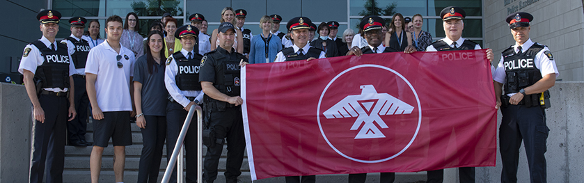 A group of people standing on steps holding up the Aninshinabek flag