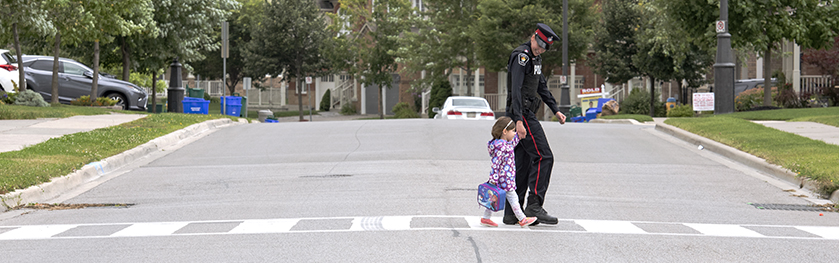 An officer and child walk across a crosswalk