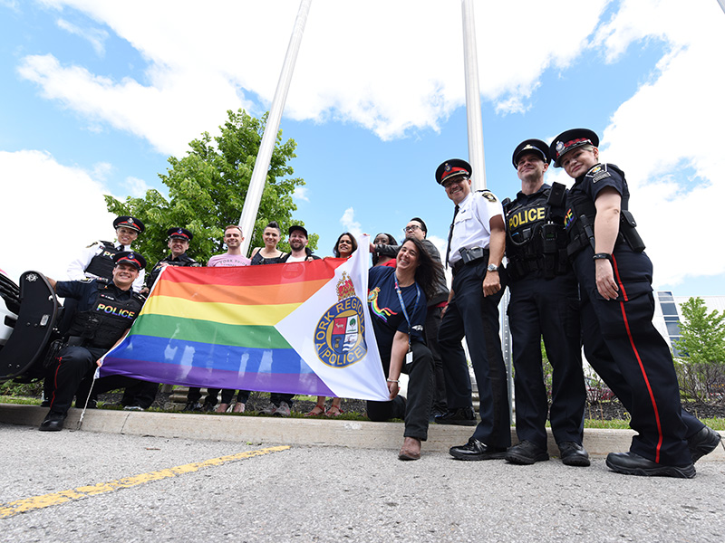 A group of officers and citizens raise a rainbow flag