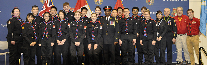 A group of teens stand on a stage with a police officer