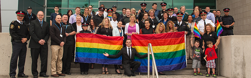 A group of officers and citizens stand together with two rainbow flags