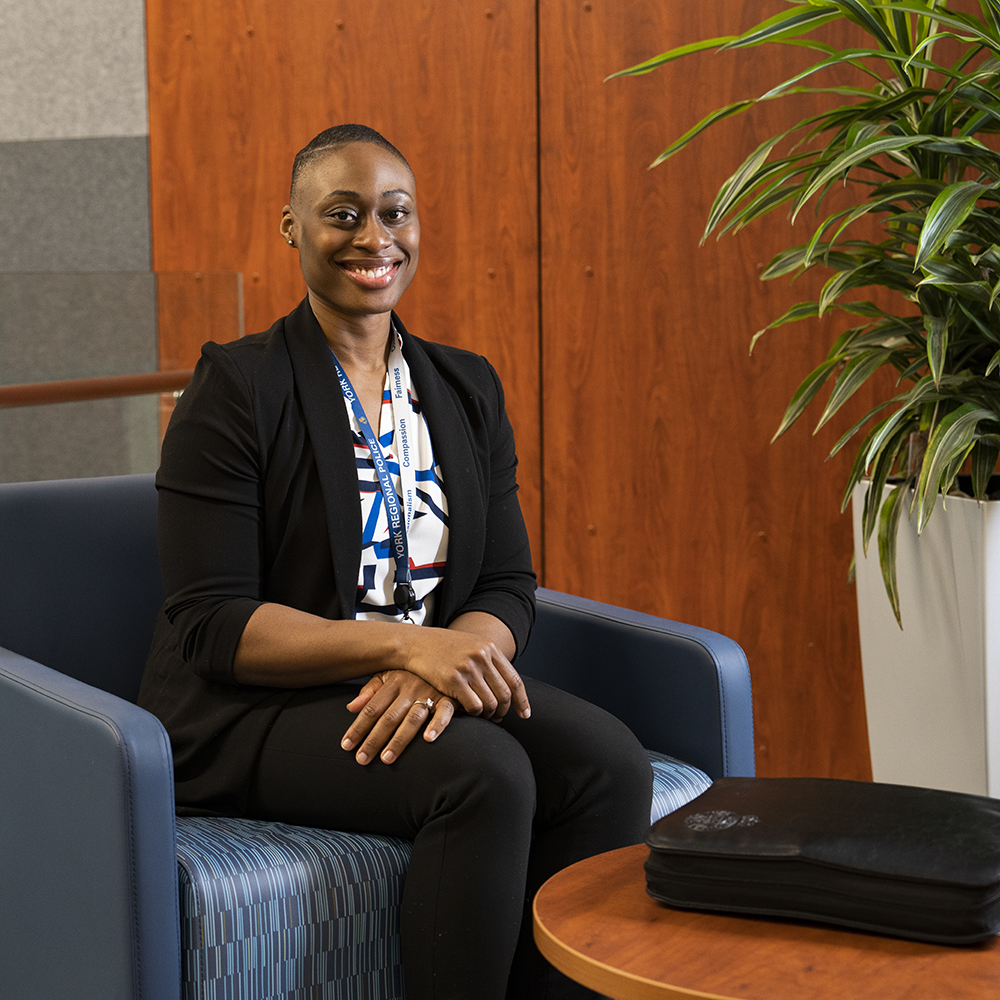 A woman sits next to a black binder, smiling