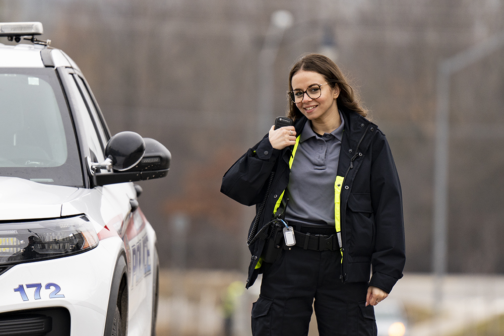 A woman talks on a radio next to a police cruiser