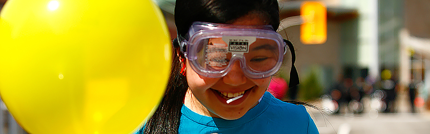 A young girl wears goggles and holds a yellow balloon