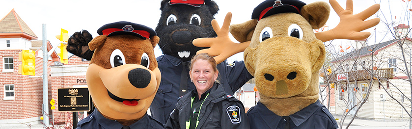 Three mascots in police uniforms, a bear, beaver and moose, pose with a female officer
