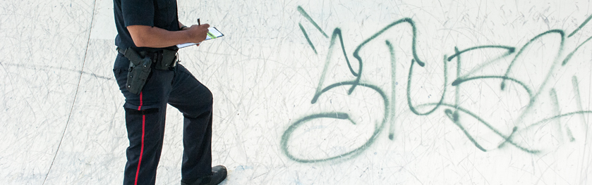 An officer writes in his notebook next to graffiti