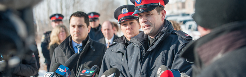 An officer speaks into a scrum of reporters