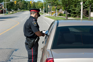 An officer stands next to a beige car