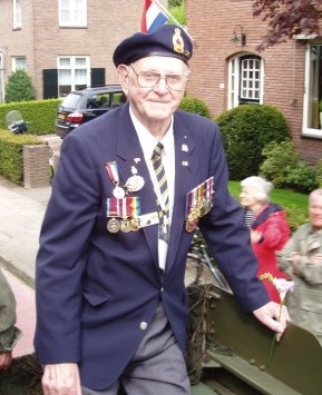 An older man stands in front of flags