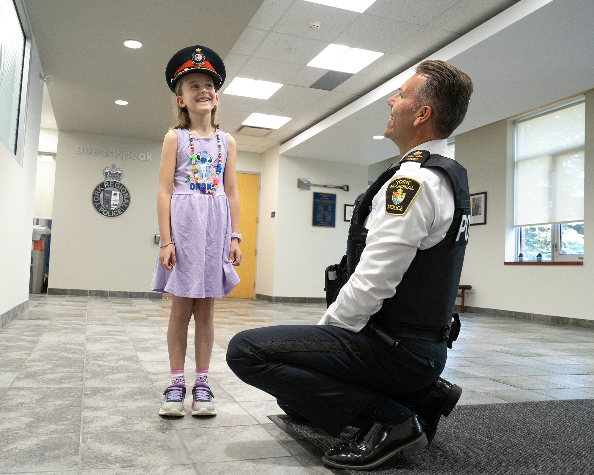 A man in a uniform squats next to a happy girl wearing a police hat