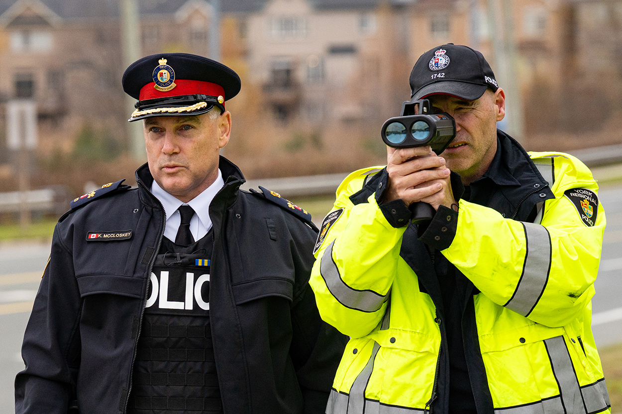 Two men in police uniforms, one looking through the viewfinder of a device