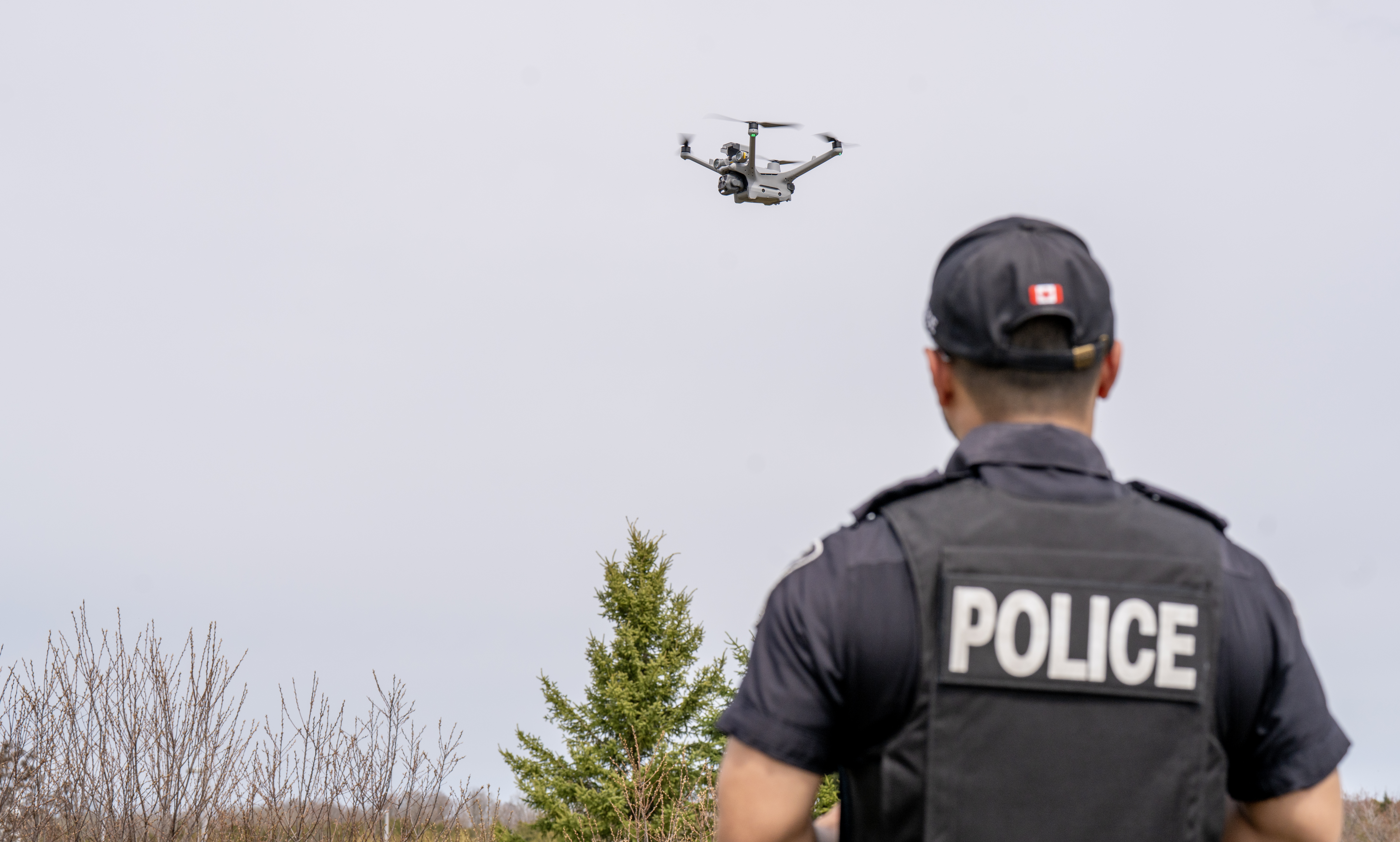 A man in a police uniform holds a controller next to a drone