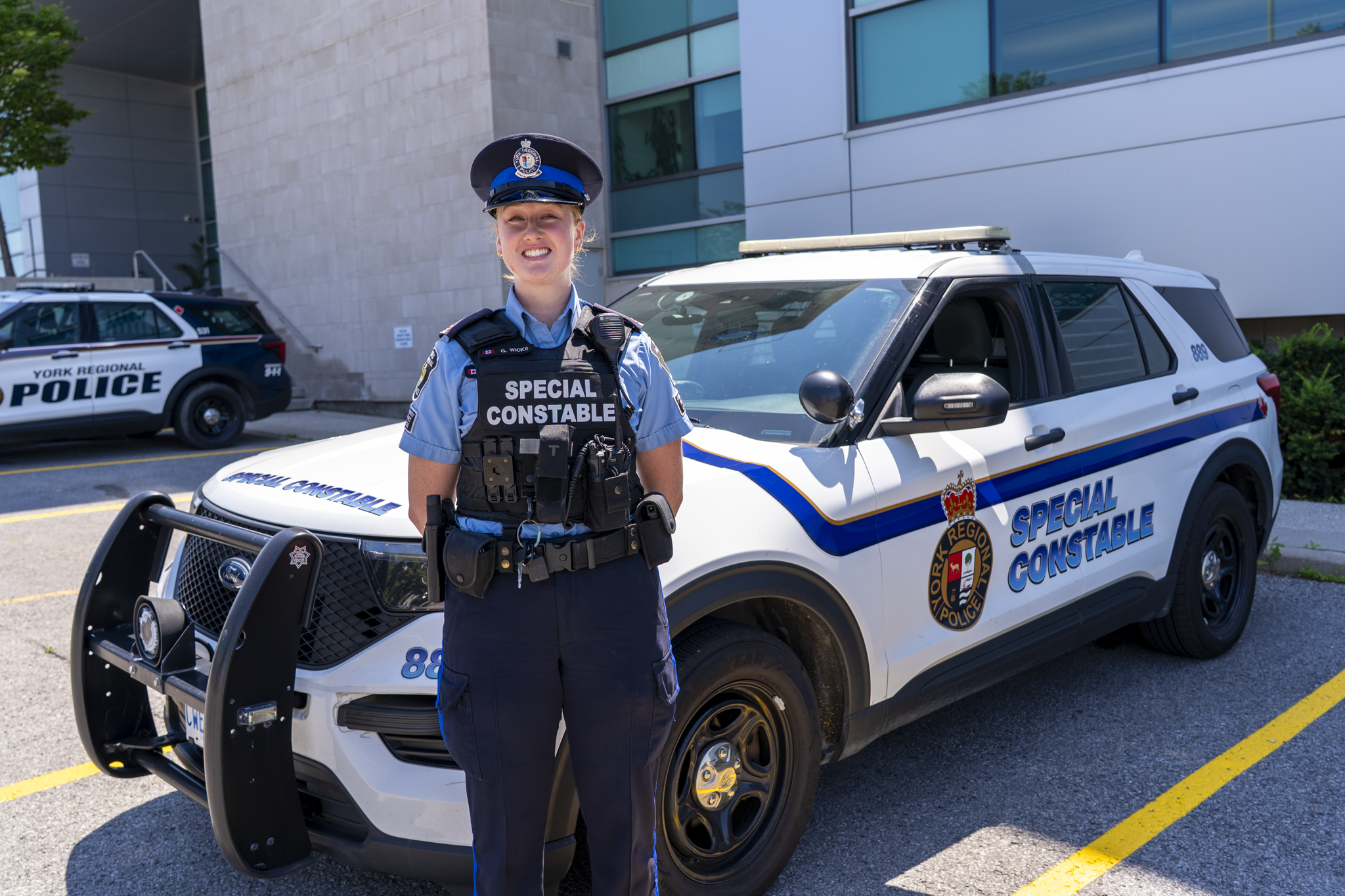 A female police special constable stands in front of a police car smiling