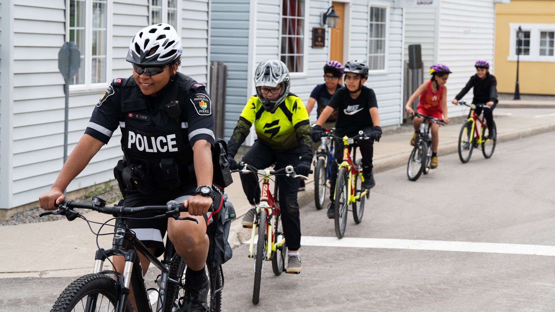 A woman in a police uniform leads children on bicycles