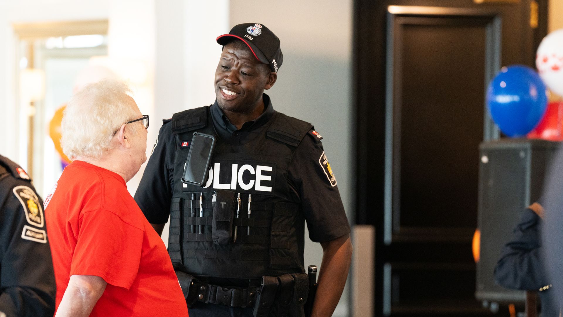A man in a police uniform speaks to a woman in red