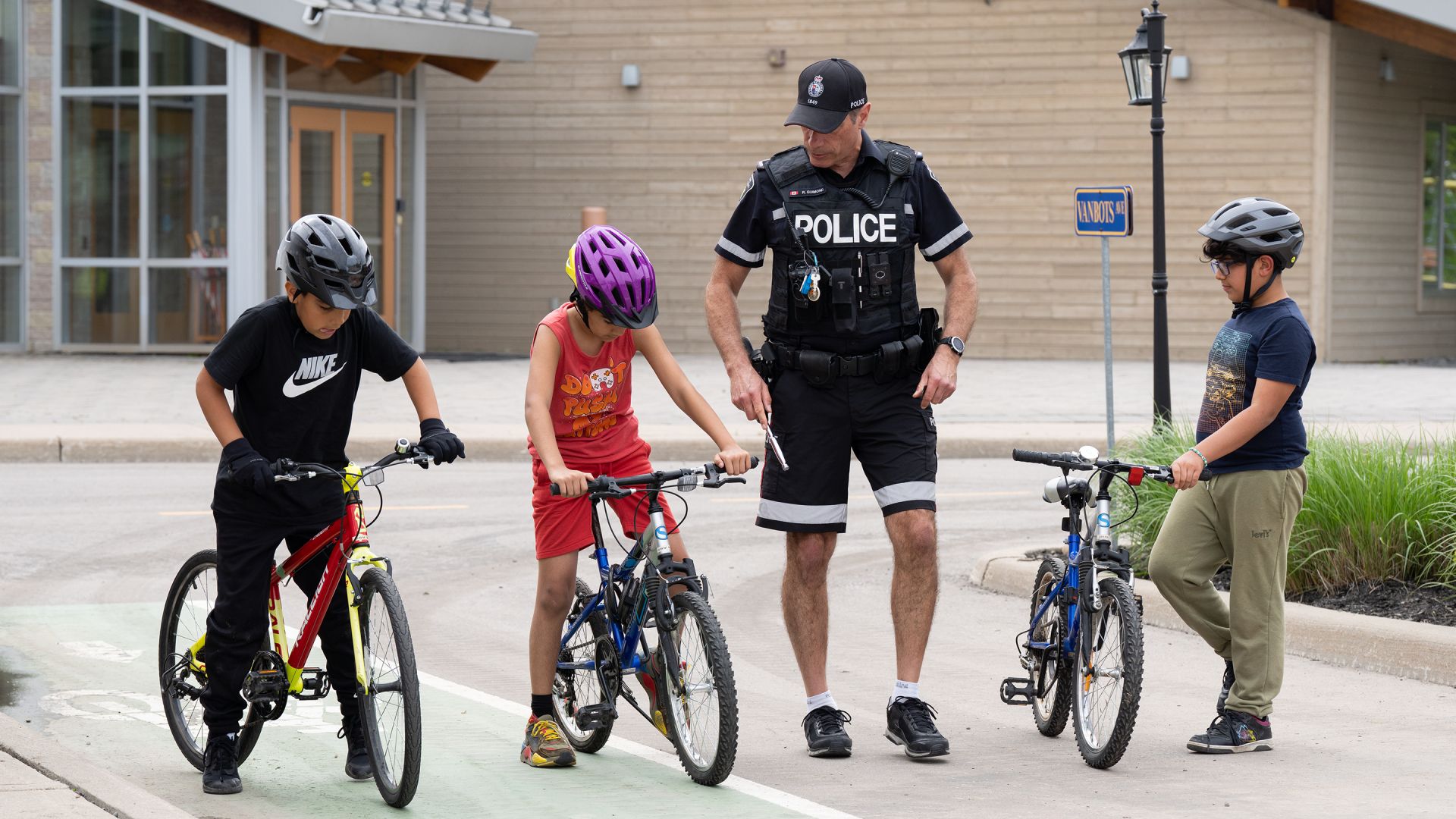 A man in a police uniform and three children look at their bicycles