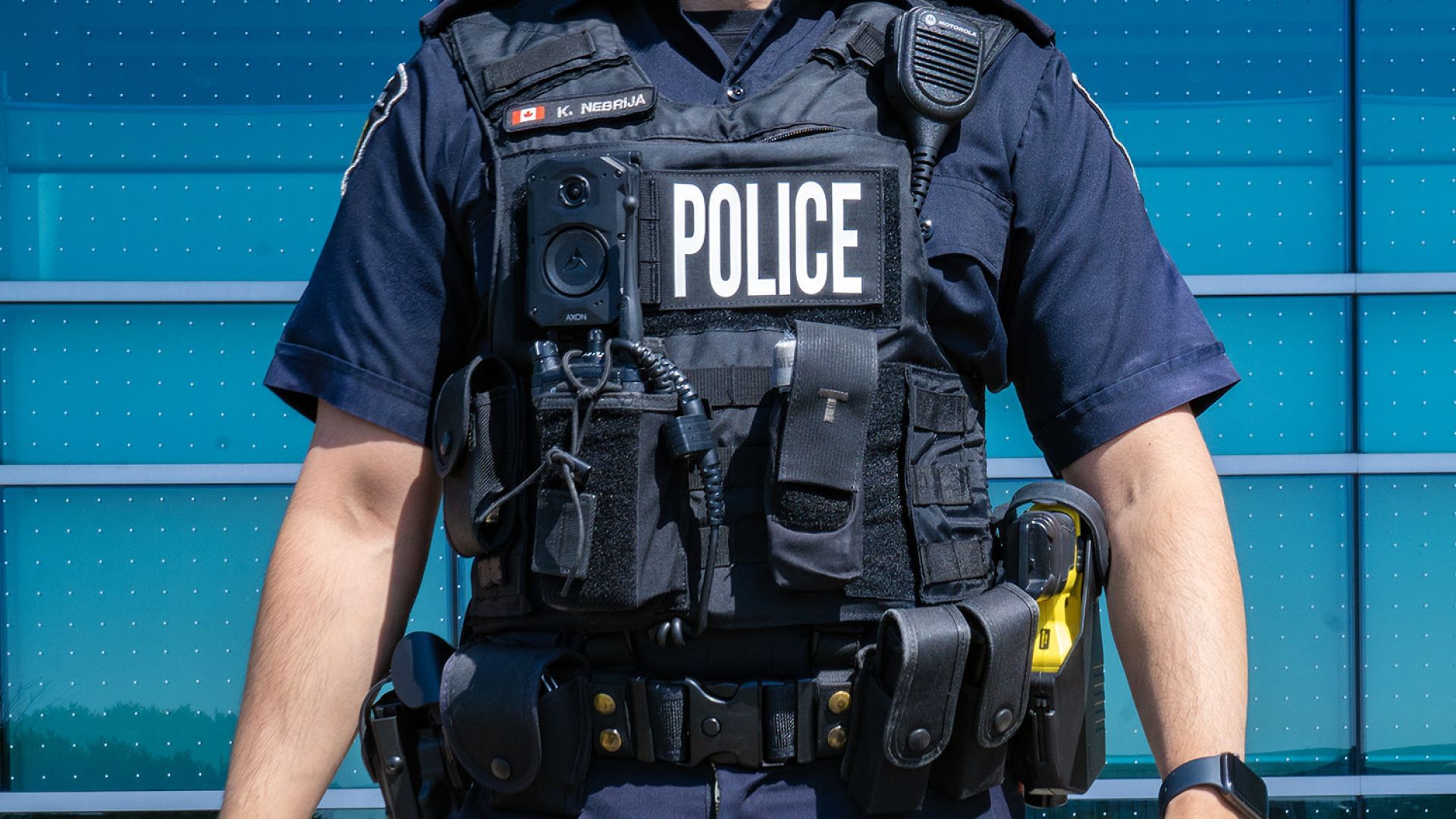 A man in a police uniform wears a vest with a camera mounted to it