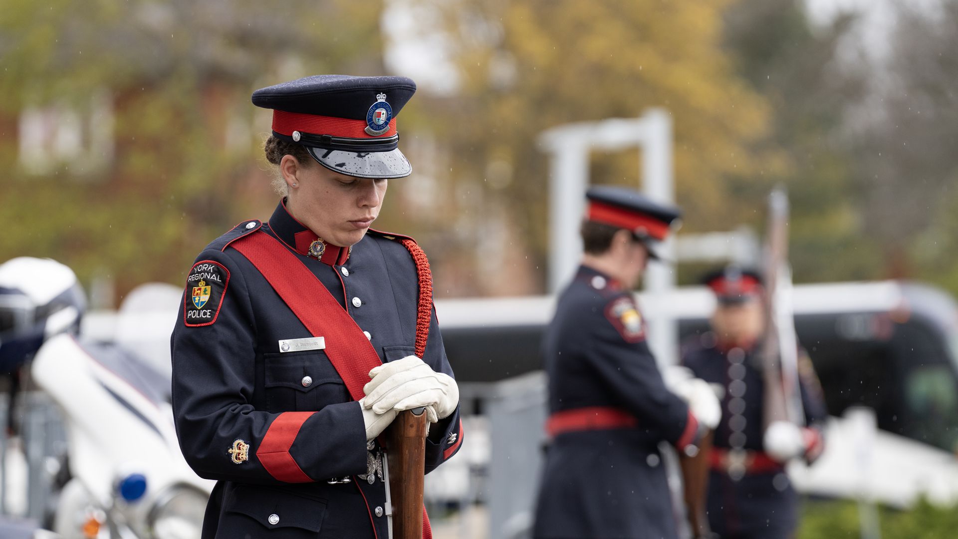 A woman in a uniform stands with head down