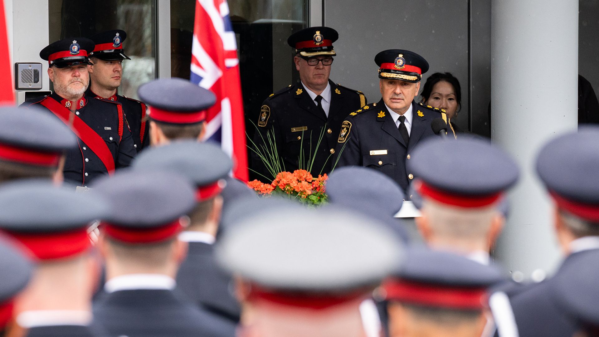 A man in a police uniform stands in front of a group of officers