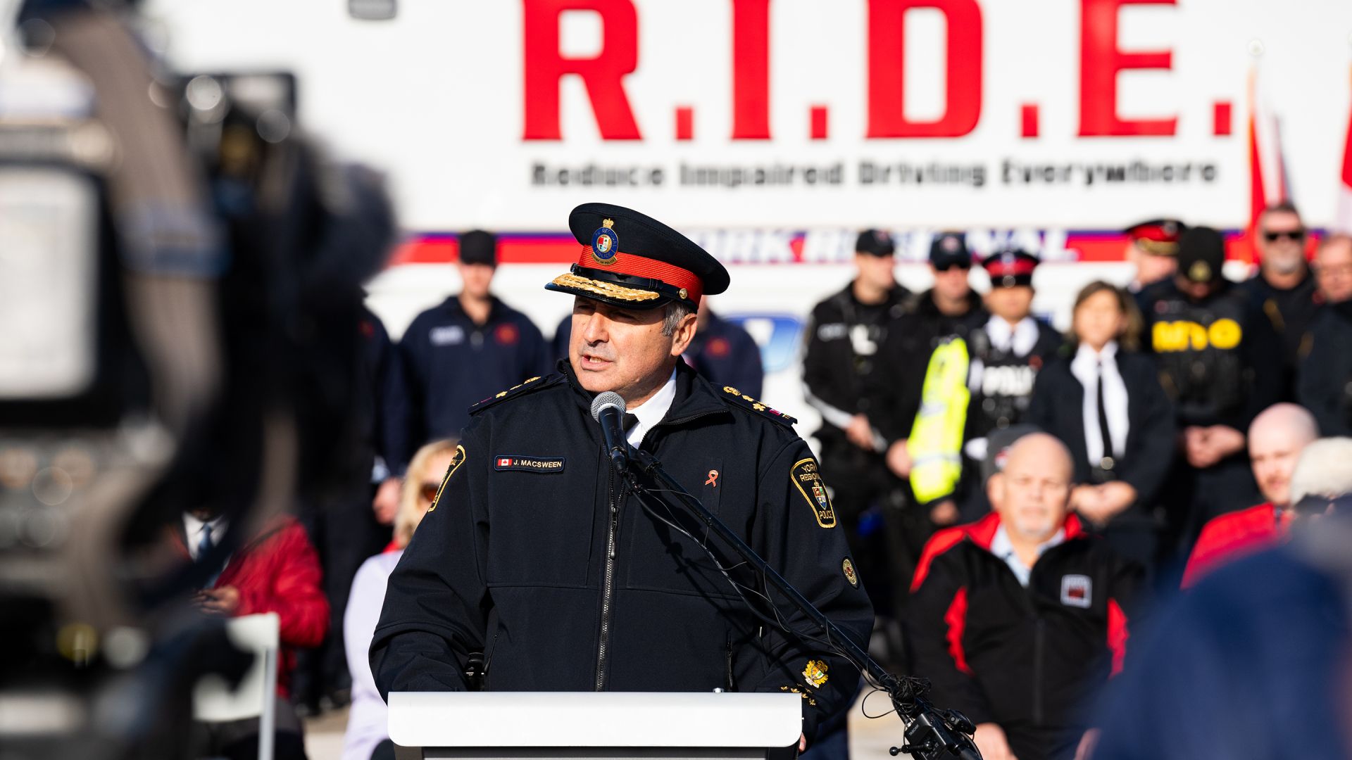 A man in a police uniform speaks at a podium in front of a RIDE sign