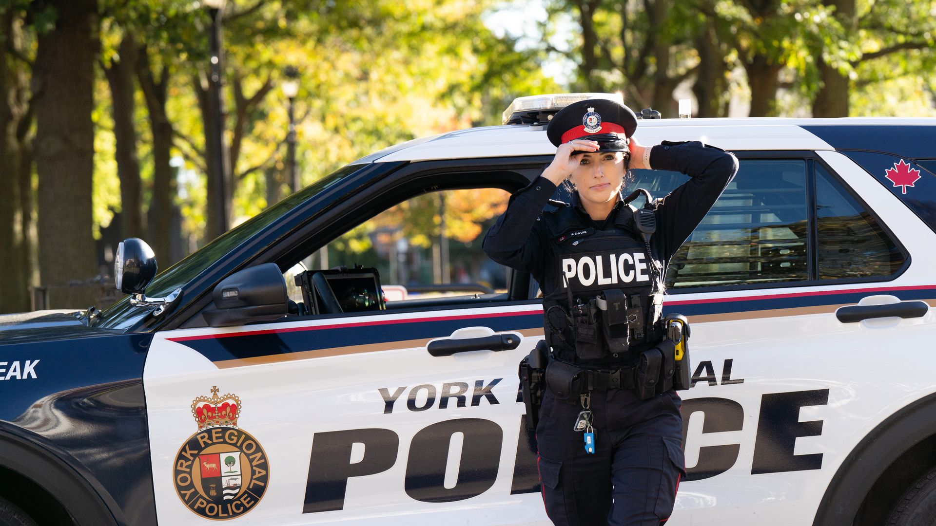 A police officer adjusts her hat in front of cruiser.