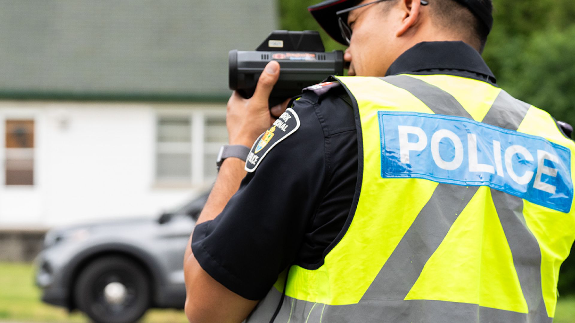 A man in a vest that reads POLICE holds a radar device