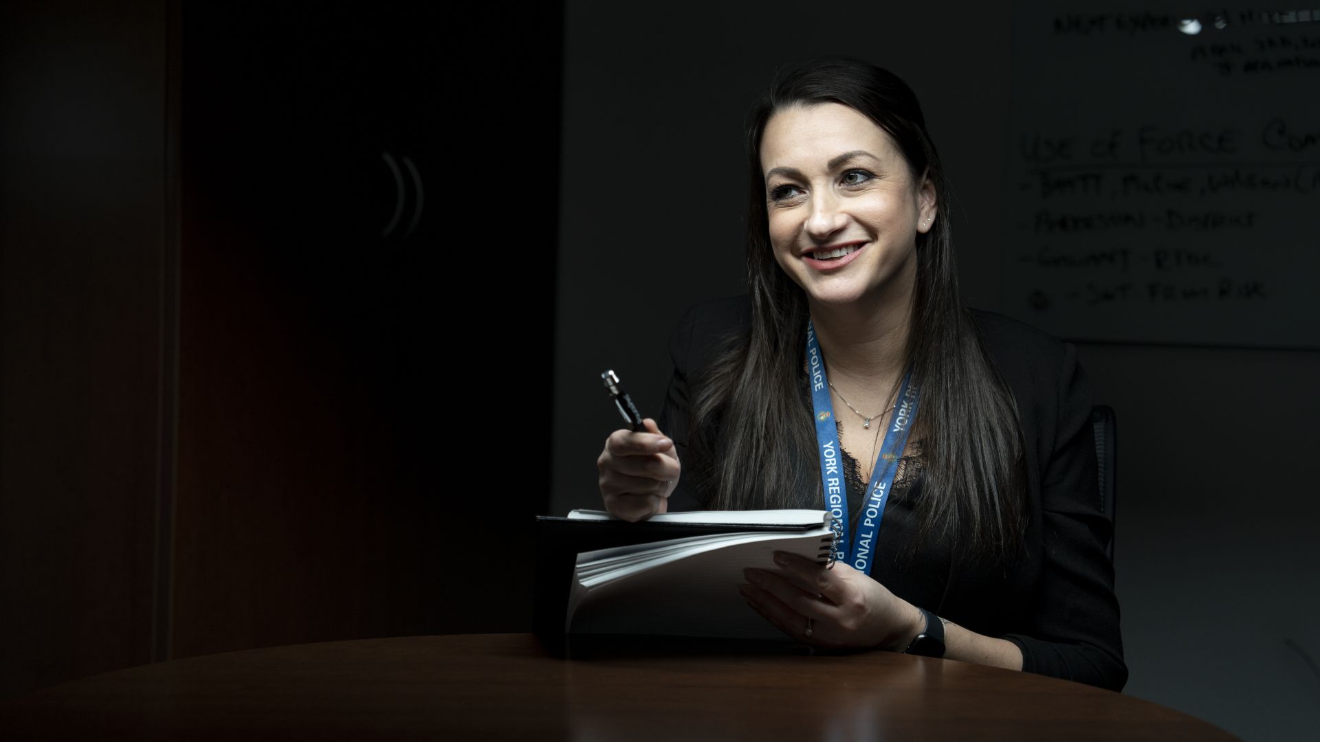 A woman wearing a YORK REGIONAL POLICE lanyard smiles while holding a pen