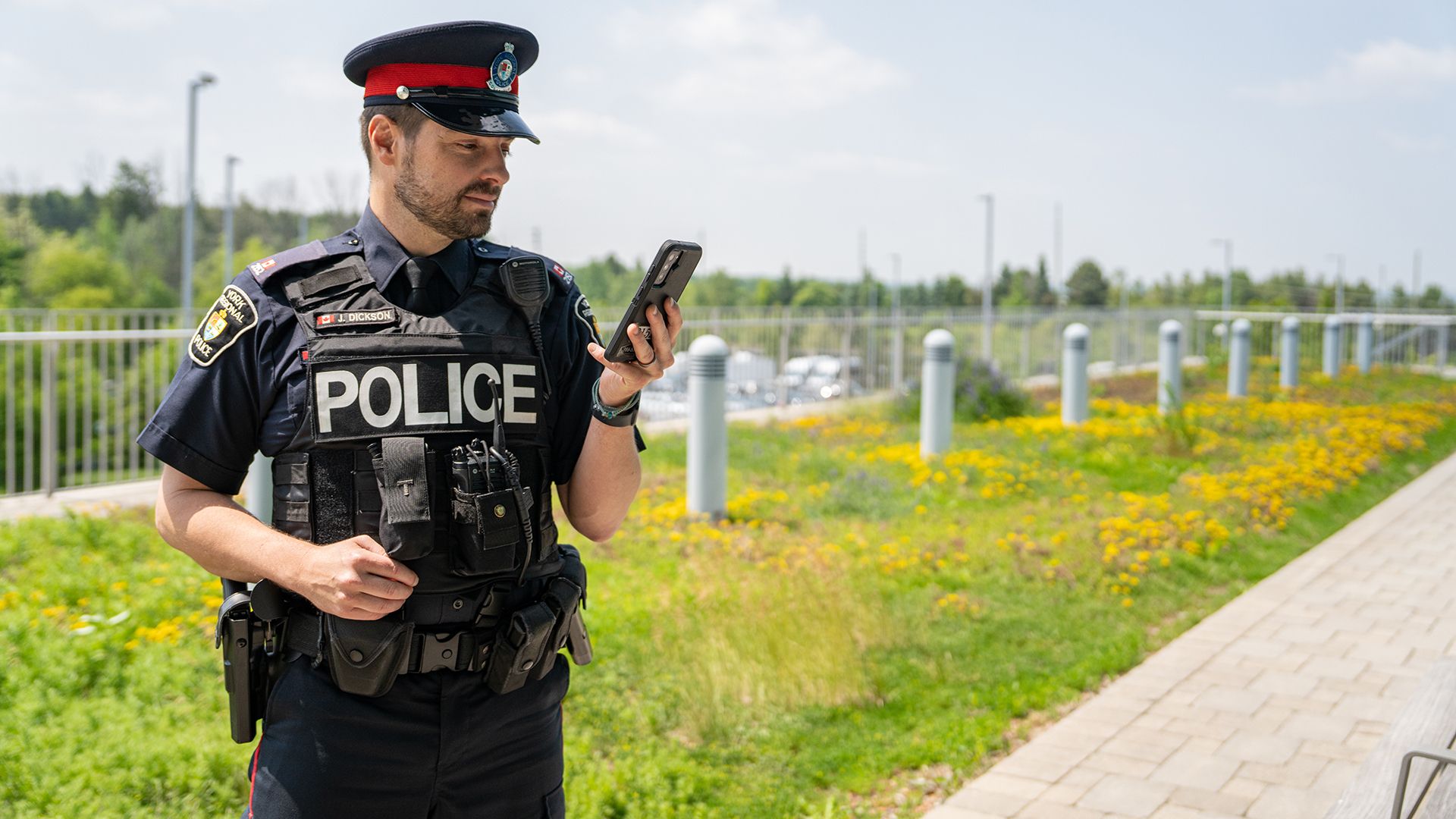 Police officer looking at phone outside on a sunny day.