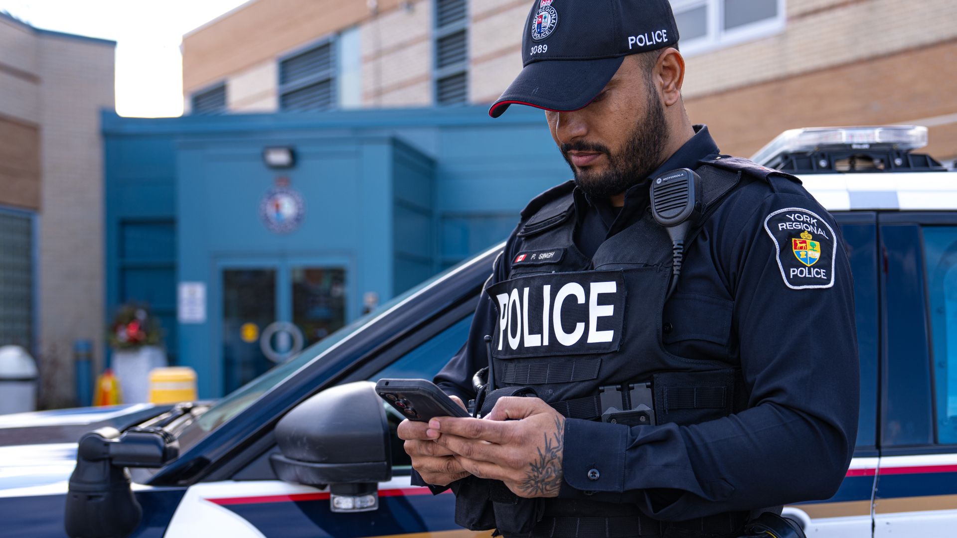 Police officer on phone in front of cruiser and police station.