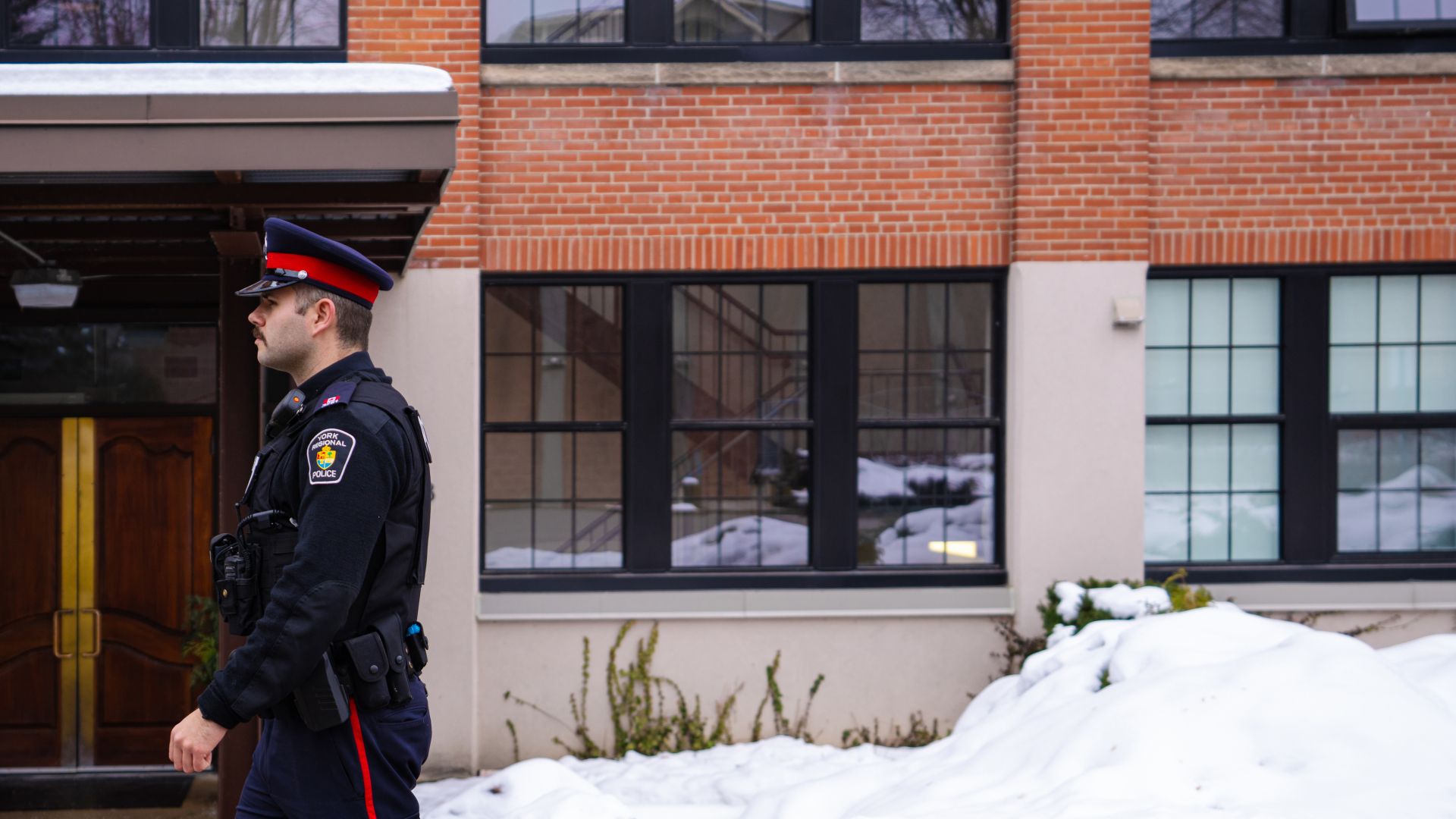 A police officer walking along the side of a building with windows.