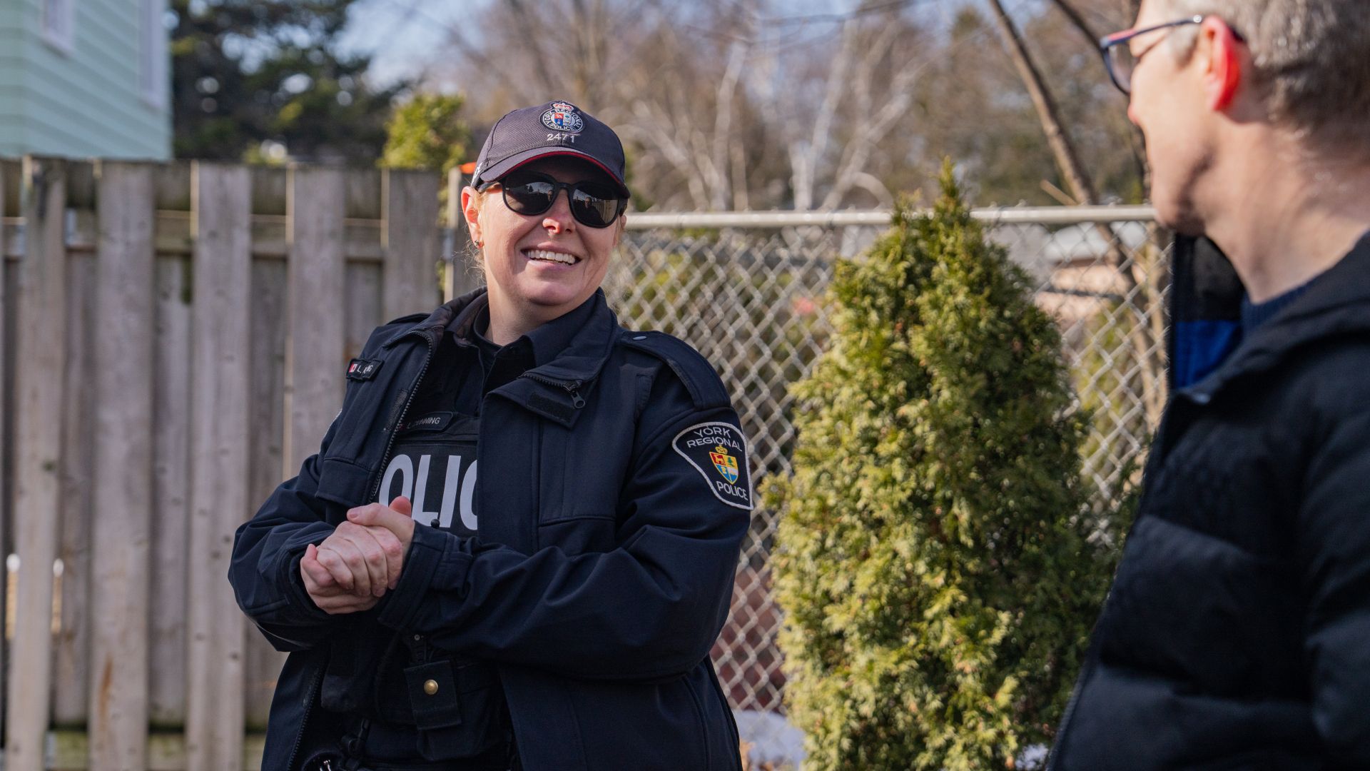 Police officer chatting with civilian in a backyard.
