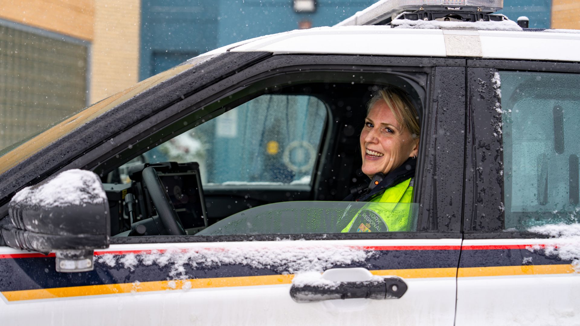 A police officer smiles from the opened window of a cruiser in the snow.