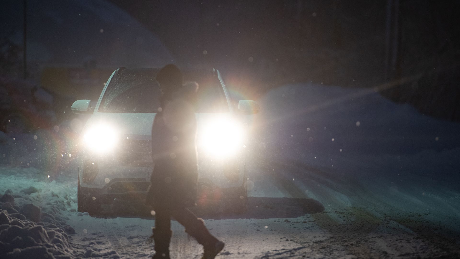 A person walks in front of a car on a snowy night