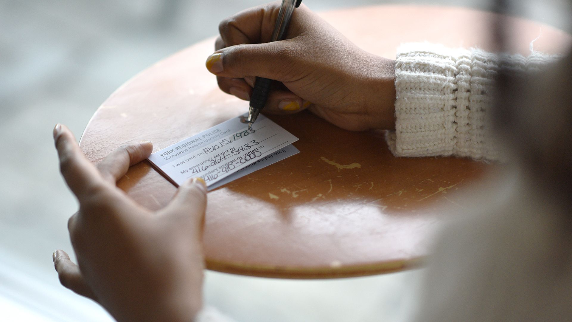 Person filling out a vulnerable person registry ID card with personal details.