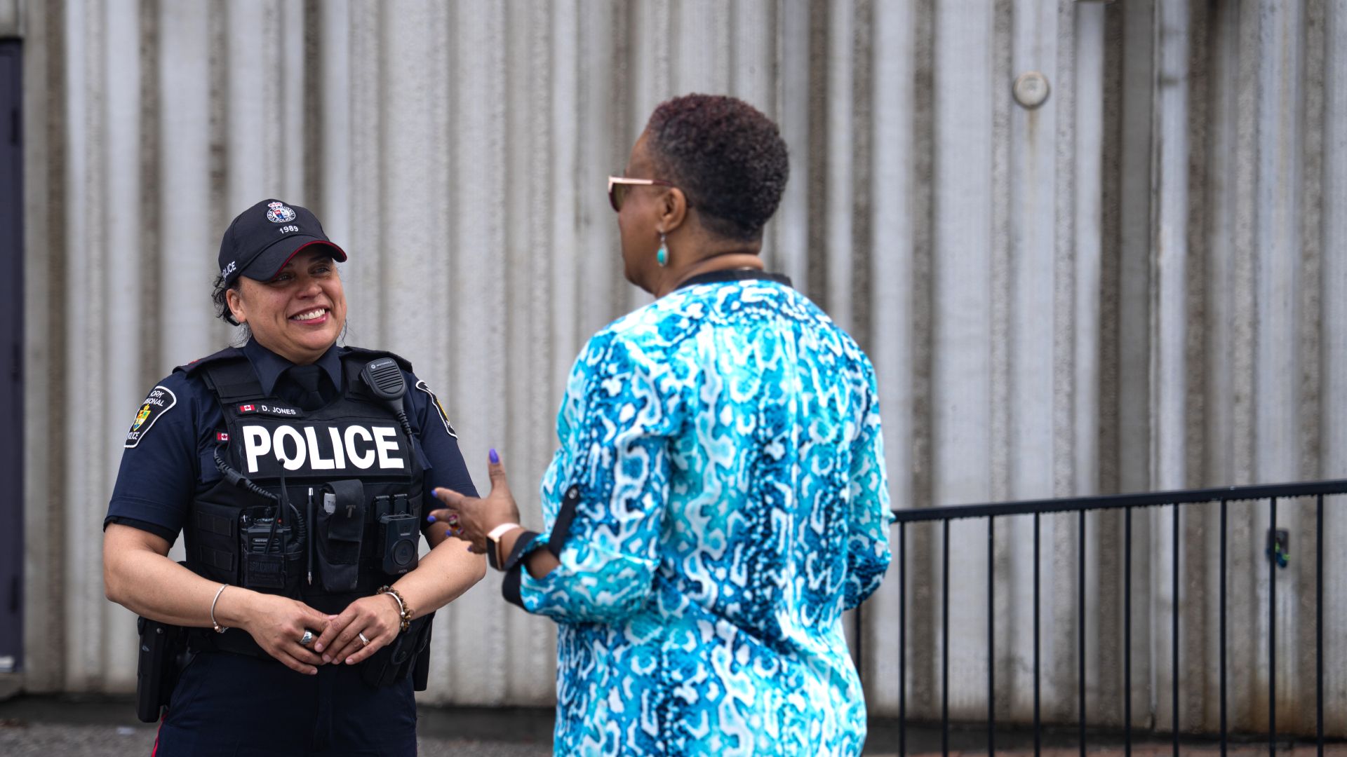 Police officer chats with a civilian woman outdoors.