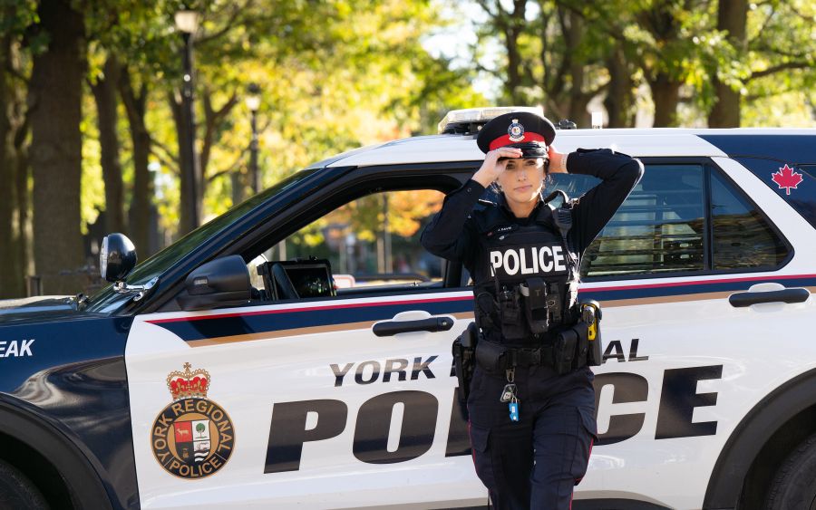 A police officer adjusts her hat in front of cruiser.