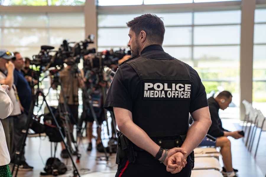 A police media officer looks over a crowd of television cameras in an atrium.