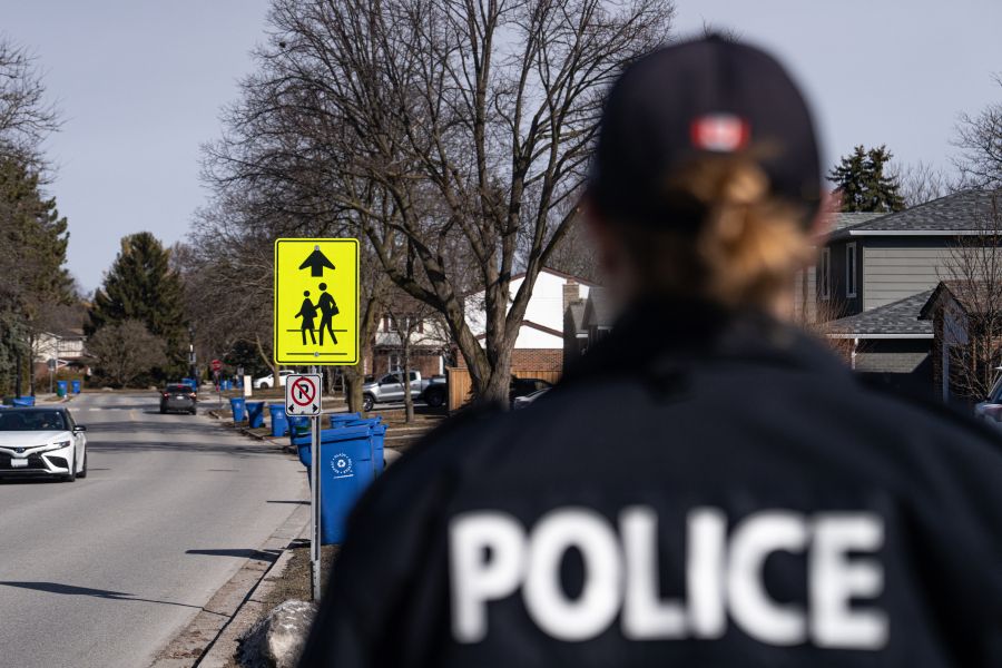 Back of police officer in foreground on a residential street with a school crossing sign in the background.