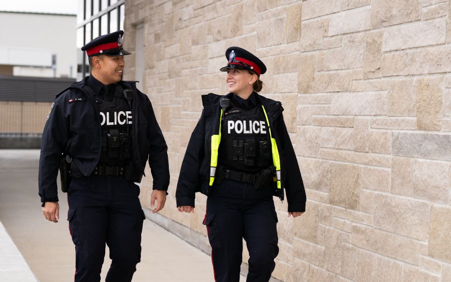 Two police officers walk and chat along a brick building.